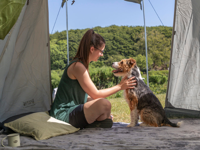 Eine Frau sitzt mit ihrem Hund zusammen auf einer grauen Decke in einem Zelt.