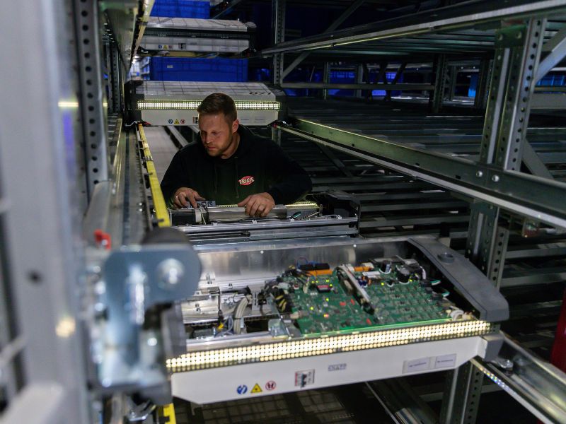 Anlagentechniker schraubt an einer technischen Anlage im automatischen Lagerregal.