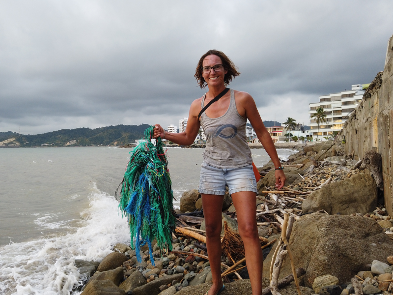Woman standing on a rocky shore holding an old fishing net/ghost net.