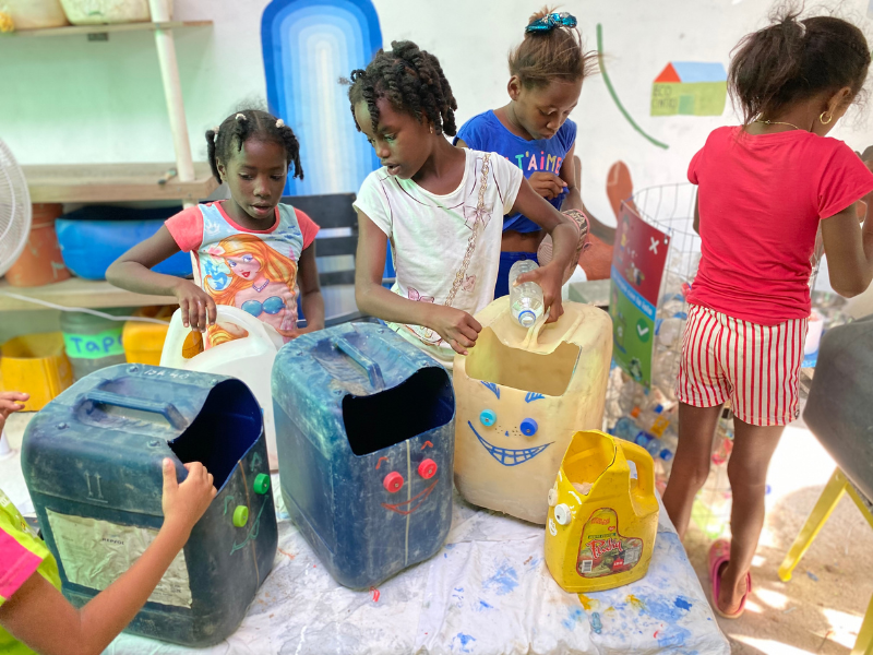 Kinder bauen aus 5 Liter Plastikcontainern Spielzeuge und verziehen sie mit Gesichtern.