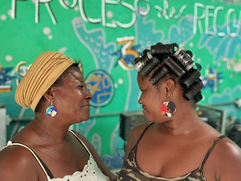 Two women present earrings and curlers made from recycled plastic
