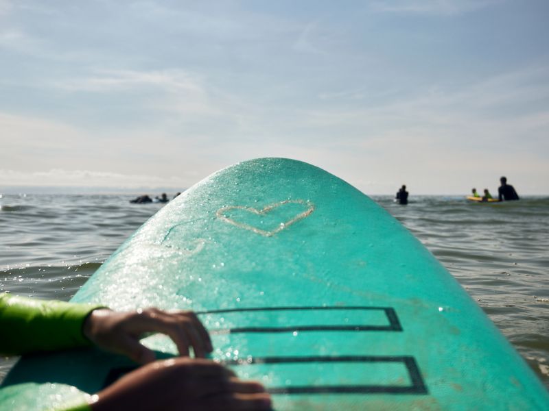 A wax heart can be seen on the tip of the light blue surfboard.