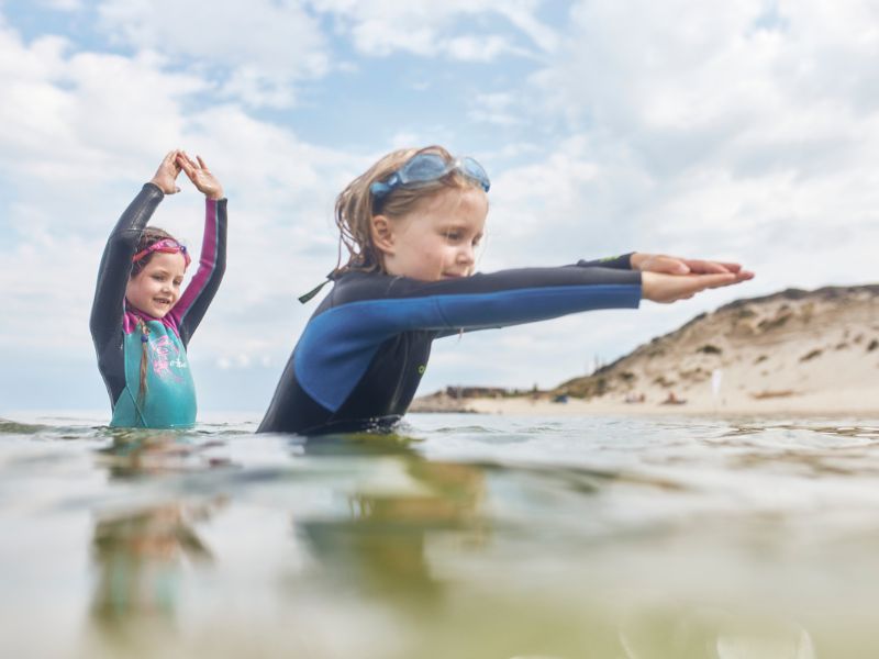 Two children are standing in water up to their waists and stretching out their arms.