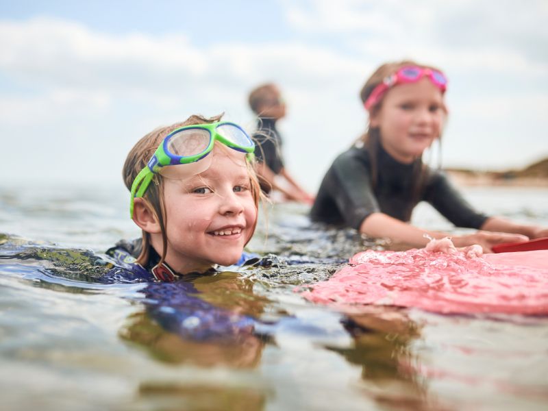 Two children are swimming in the sea and laughing at the camera.