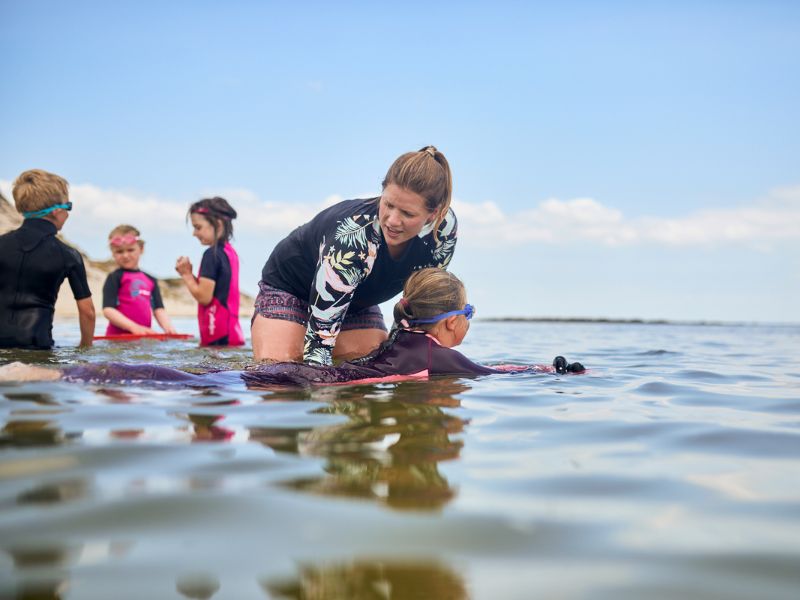 A swimming instructor is helping a child swim in the sea while lying on his stomach.