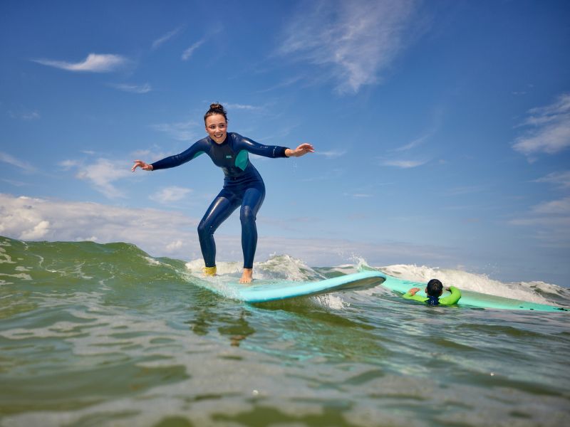 A girl stands on a surfboard and rides a small wave. 