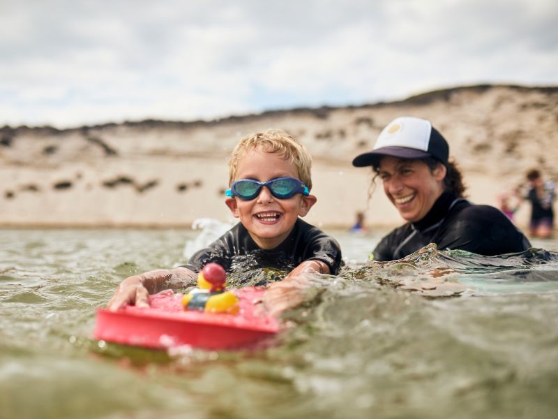 A little boy wearing swimming goggles is being helped to swim in the sea.